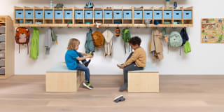Zwei Kinder sitzen vor einer Kita-Garderobe auf Gardeorbenbänken und ziehen sich ihre Schuhe an.