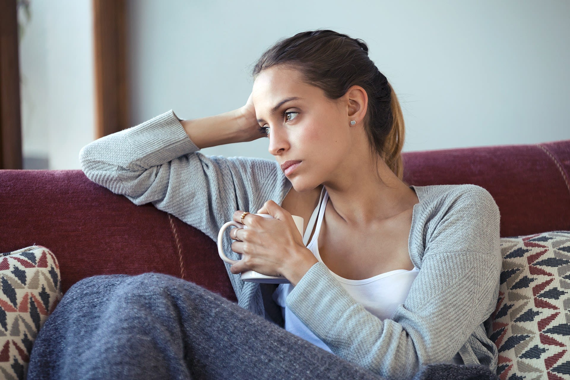 Schwangerschaft | SSW 7 | Frau, die über ihre Probleme nachdenkt, während sie auf dem Sofa zu Hause Kaffee trinkt