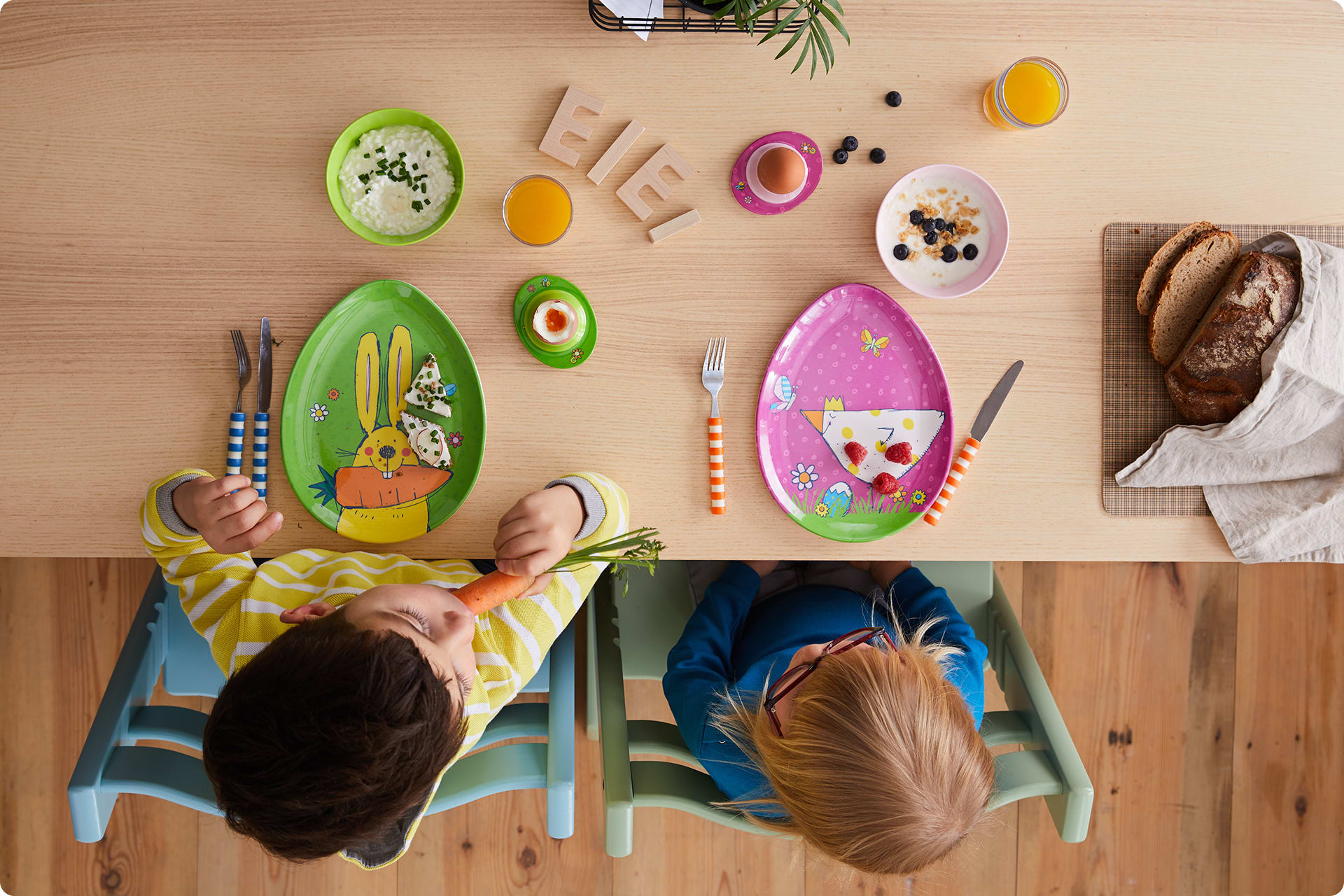 Osterrezepte für Kinder |  zwei Kinder sitzen am Tisch, vor Tellern in Ei-Form mit Ostermotiven