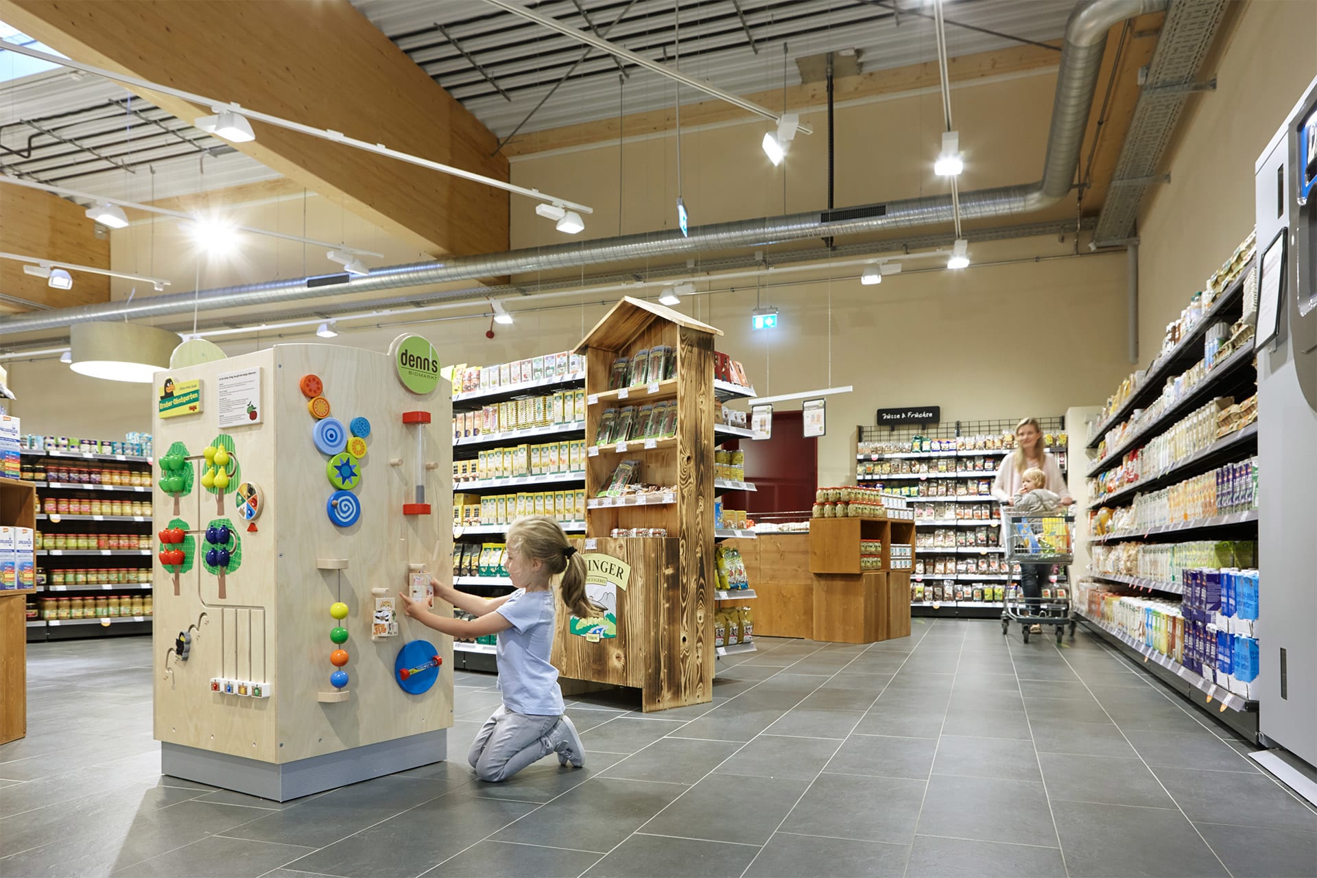 Branchen | Business | Verkaufsfläche Kind spielt an einem großen Spielwürfel Mutter mit Einkaufswagen im Bildhintergrund