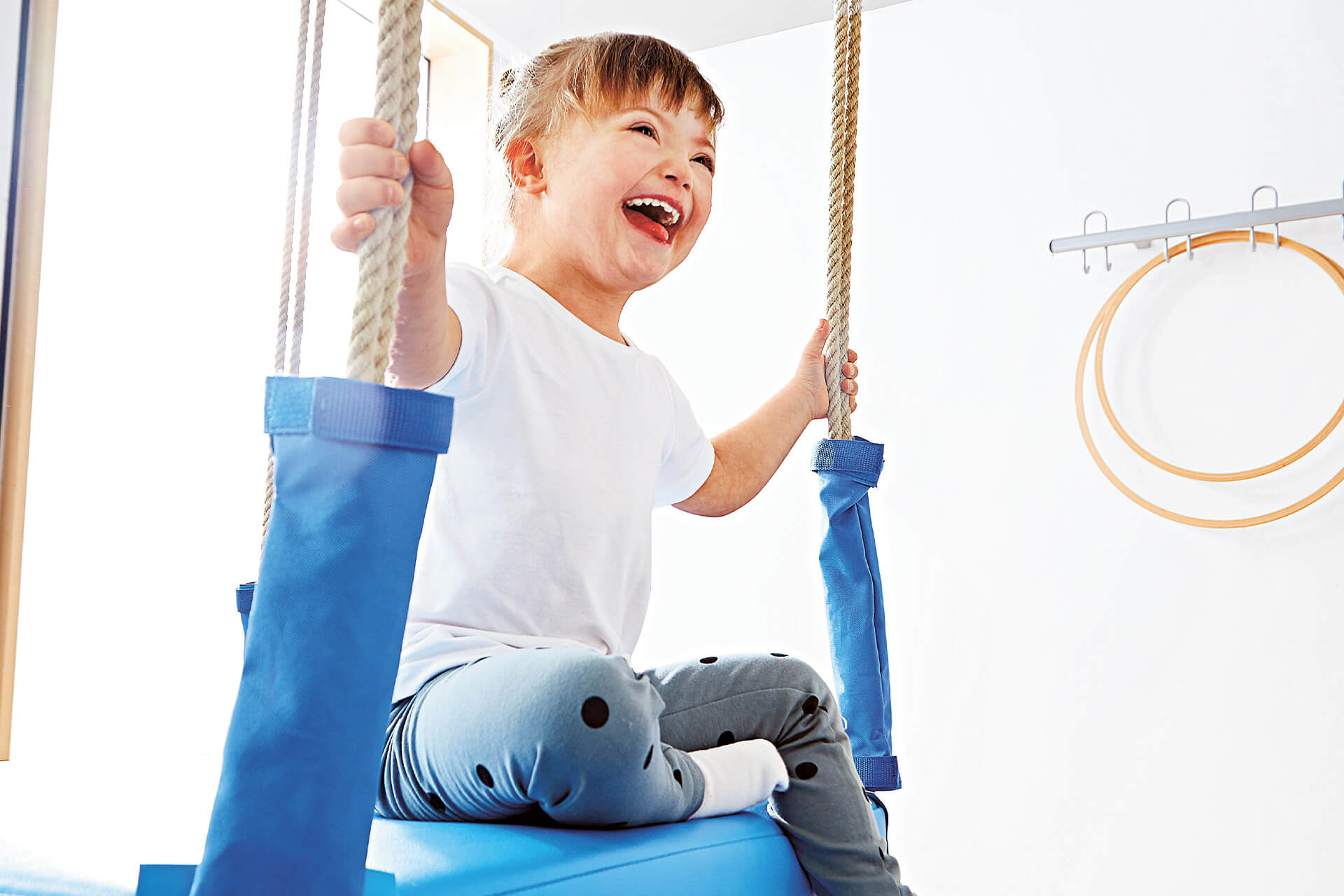 Business | Healthcare | 2 | Image | Ziele & Bedürfnisse | Junge mit Downsyndrom sitzt auf einer blauen Schaukel