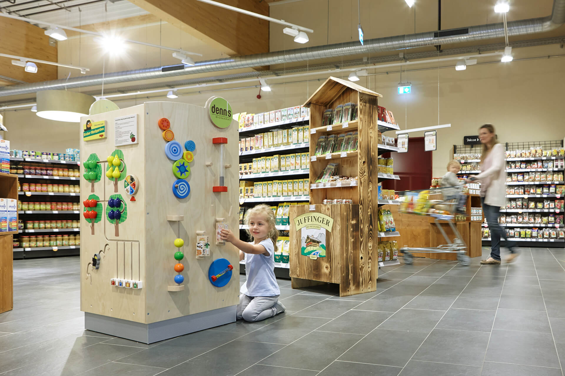 Retail | 2 | Ziele und Bedürfnisse | Kind kniet vor einem großen Spielwürfel, der im Supermarkt steht