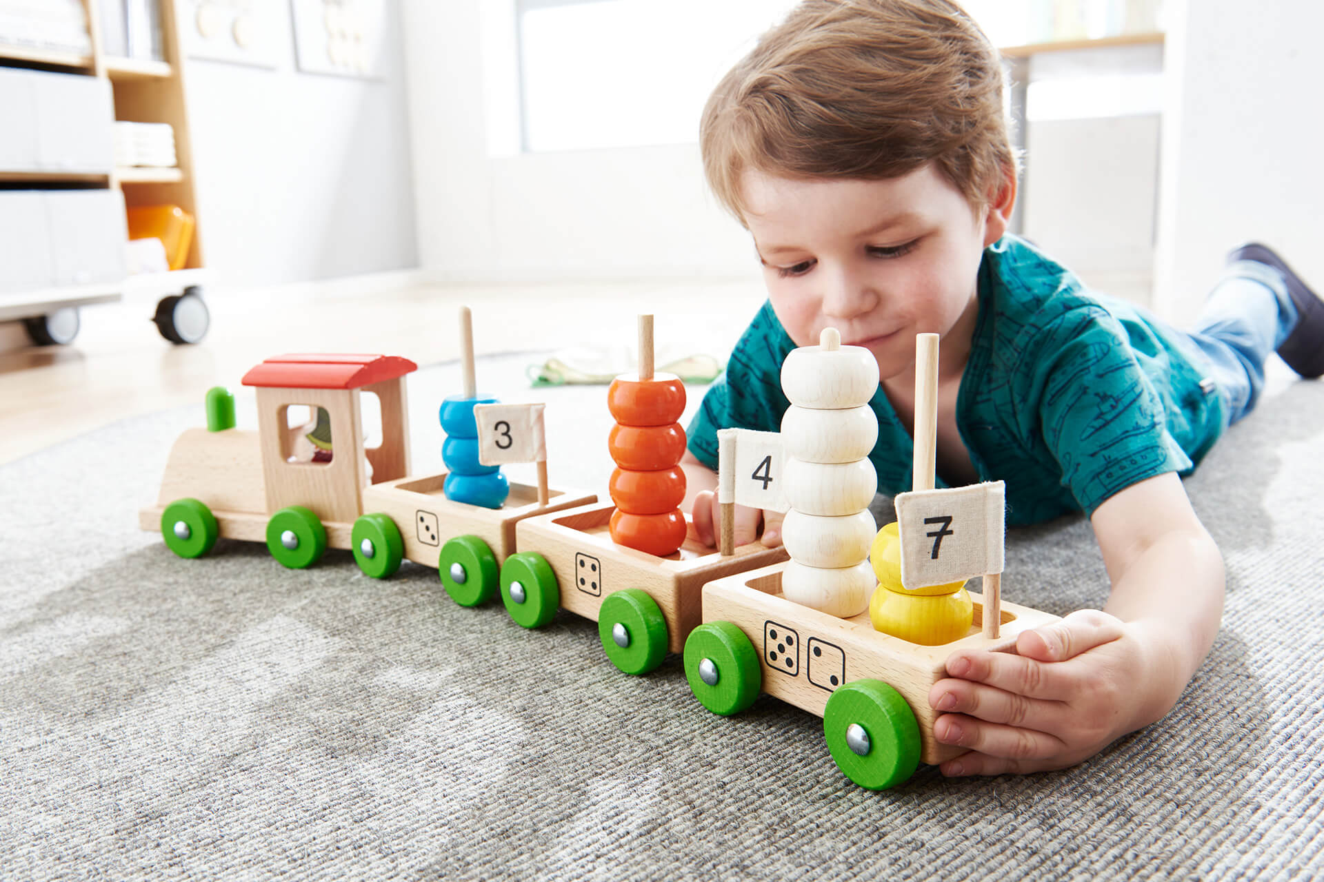 Bildung | Kindergarten | 2 | Image | Junge liegt auf dem Bauch und spielt mit einer Holzeisenbahn