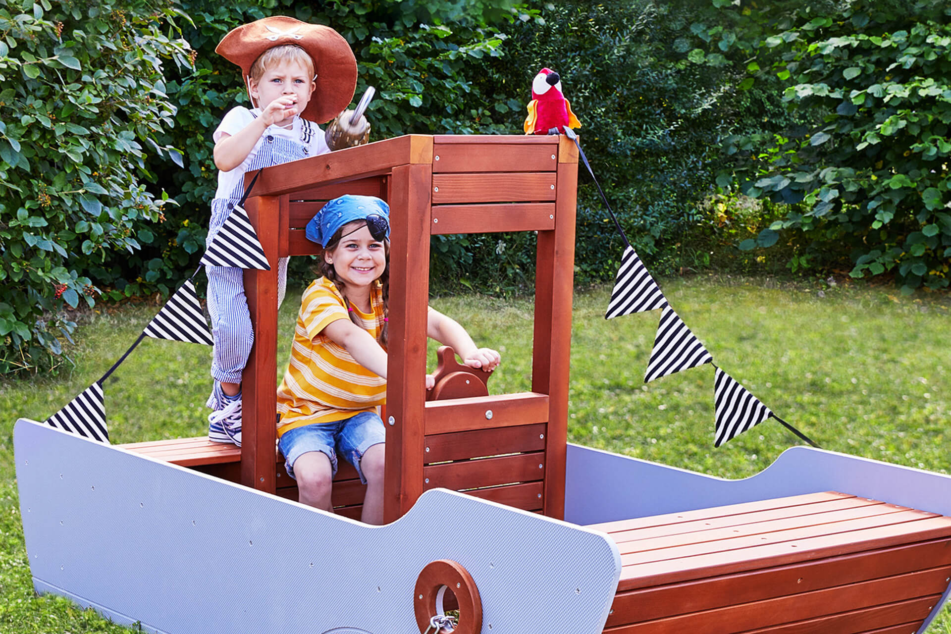 Education | Kindergarten | 2 | Image | Outdoorspielzeug | Mädchen mit blauen Hut sitzt im Schiff aus Holz, Junge steht dahinter