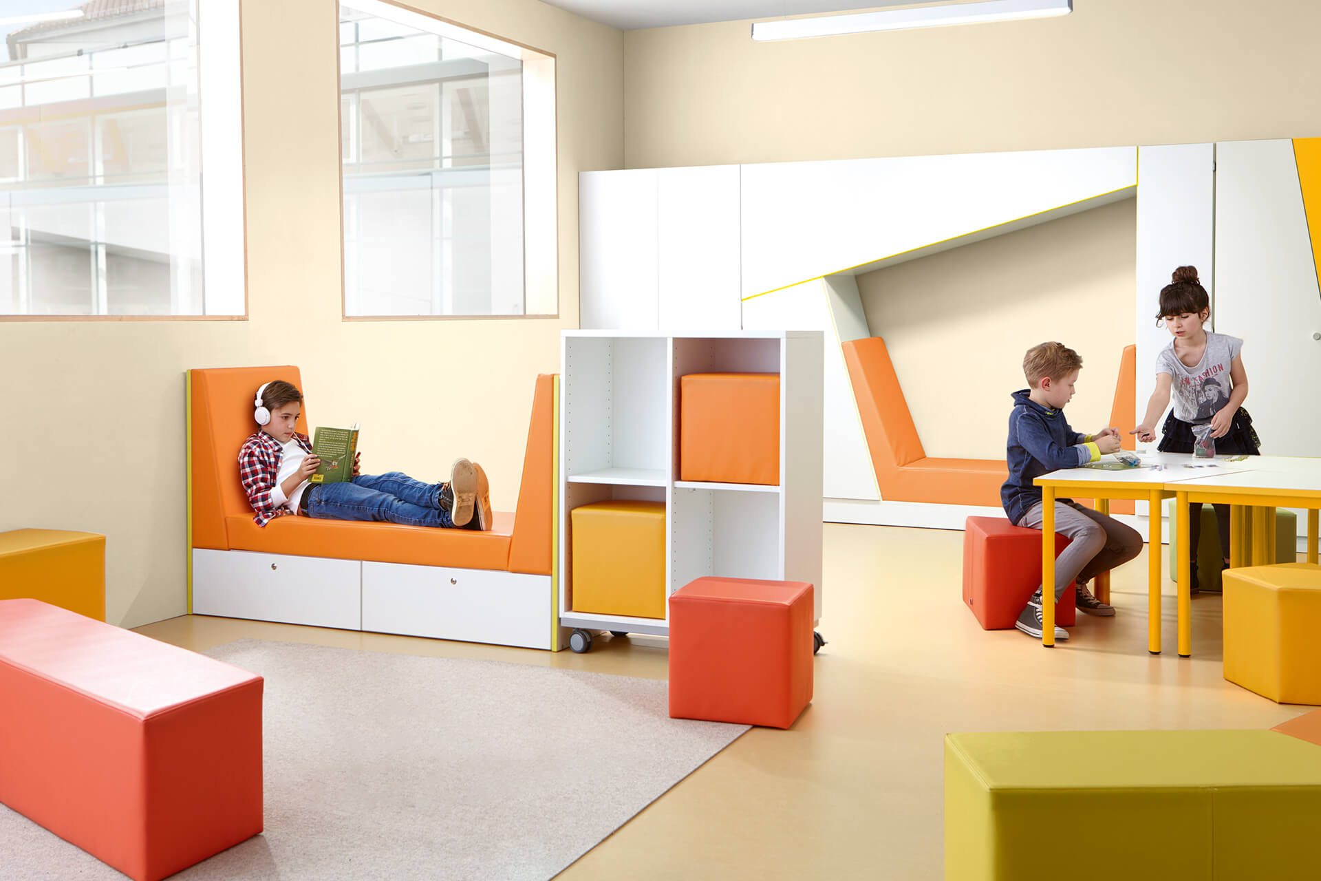 Bibliothek | Grid | 2 | Sitzlandschaften | Schüler liegt auf einem Sitzsofa und hört Musik liest dabei ein Buch