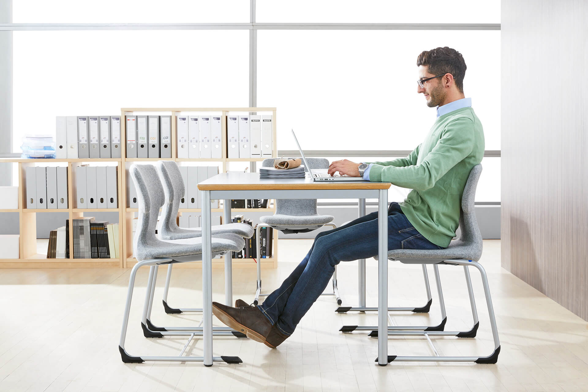 Lehrerzimmer | Grid | 2 | Stühle | Lehrer sitzt mit ausgestreckten Beinen an einem Tisch vor dem Laptop
