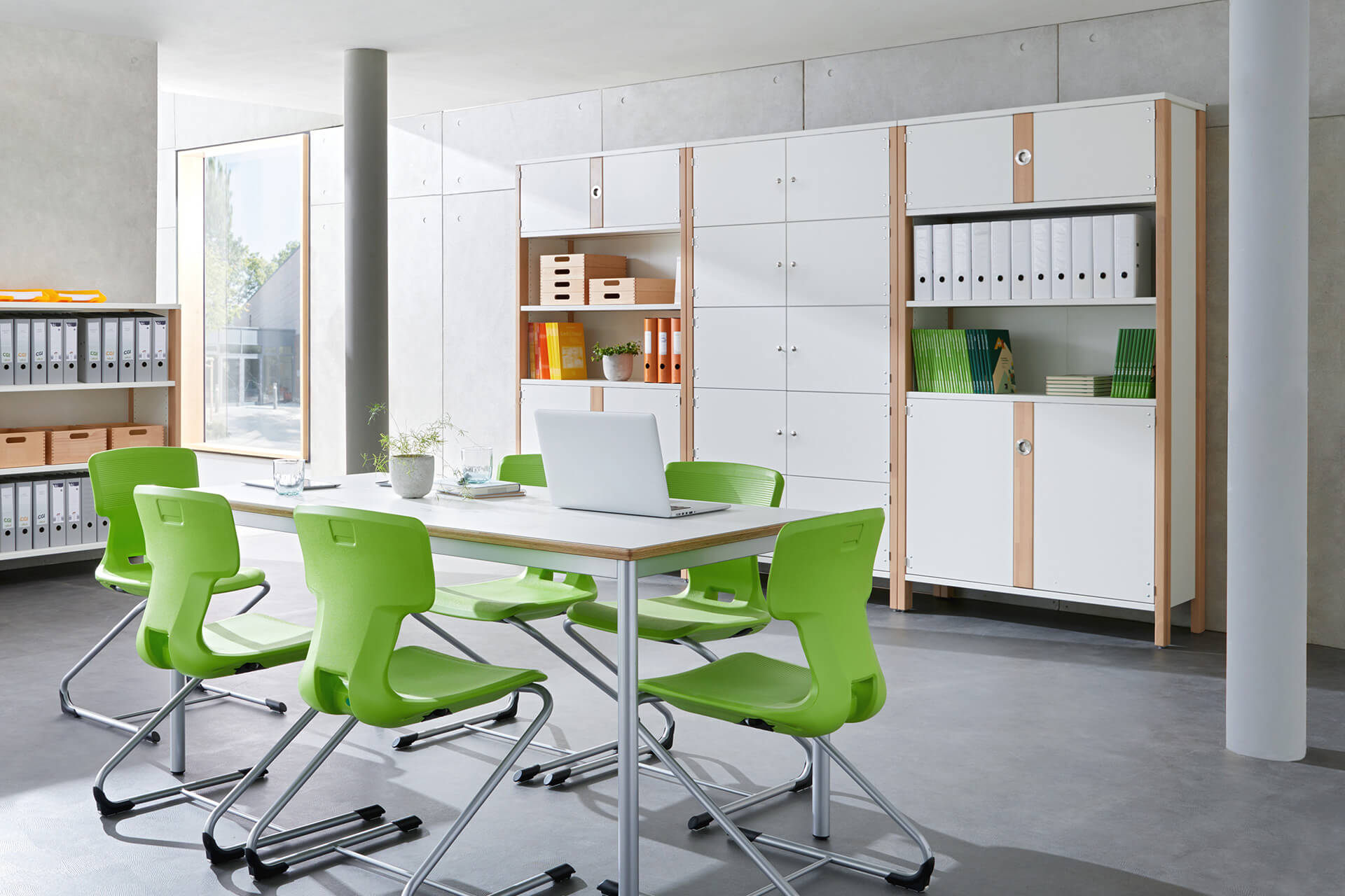 Verwaltungsraum | Schränke | Raum mit Tisch und sechs Schwingstühlen mit grünem Sitz, an der Wand stehen weiße Büroschränke mit Türen und offenem Regalen in der Mitte