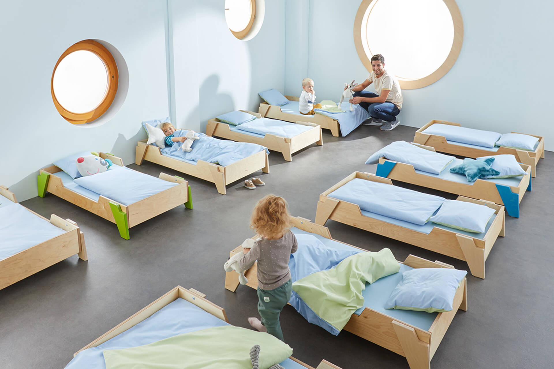 Räume | Krippe & Kindergarten | Kleine Kinder liegen in Holz-Bettchen, die in Reihe in einem Schlafsaal stehen