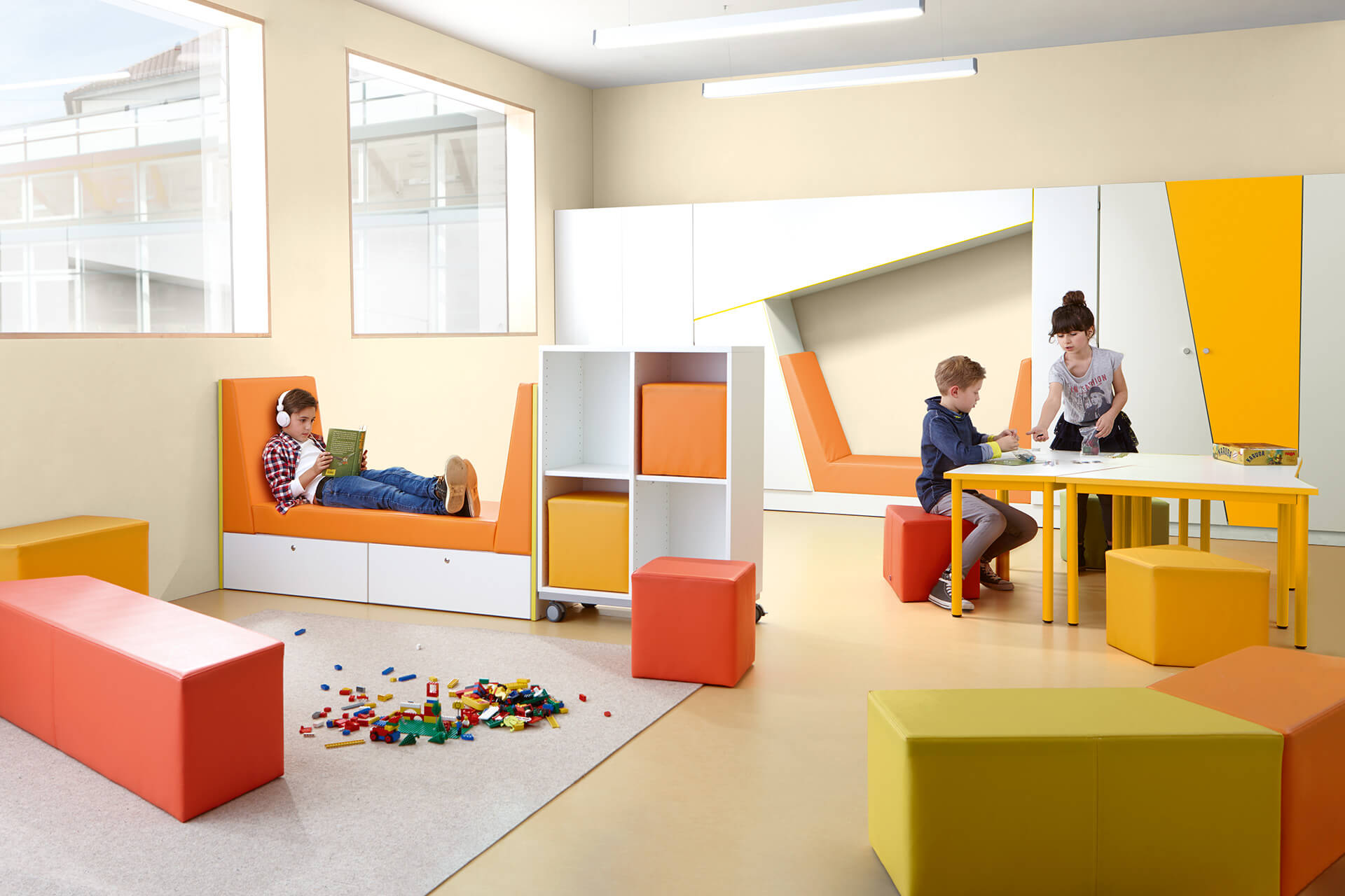 Schule & Hort |Aufenthaltsräume | Raum eingerichtet mit orange gelb, grünen Sitzmöbeln Kind sitzt am Tisch
