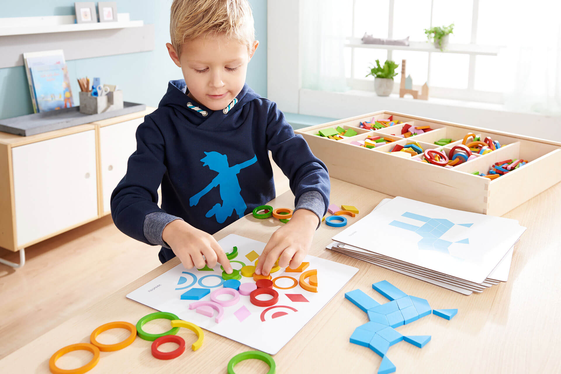 Produktreihen | Kind mit blauen Pulli legt ein Bild mit Ringen 