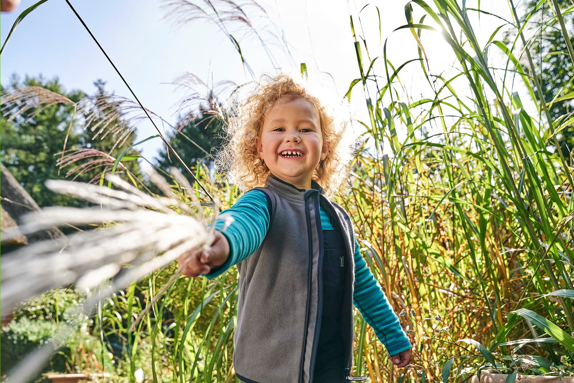 Über uns | Nachhaltigkeit | Kleines Kind mit Fleece-Weste steht im hohen Gras