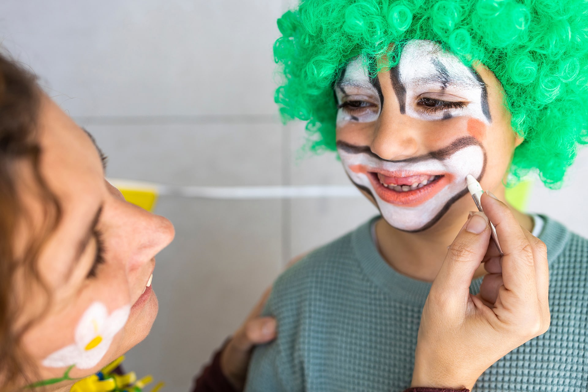 Faschings schminken | Image | Kind mit grüner Clownsperücke wird im Gesicht als Clown geschminkt