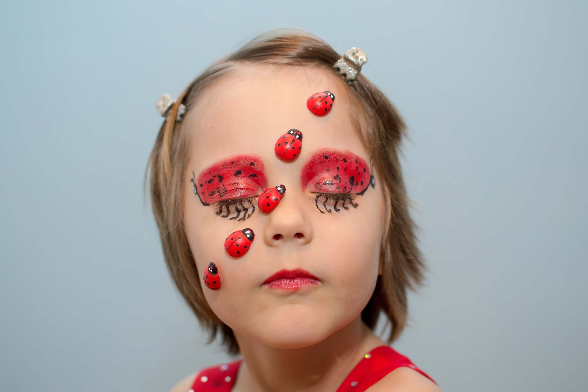 Faschings schminken | Image | Mädchen als Marienkäfer im Gesicht geschminkt - Augenlider rot mit schwarzen Punkten. Plastische Marienkäfer sind aufgeklebt, quer über Wange und Stirn