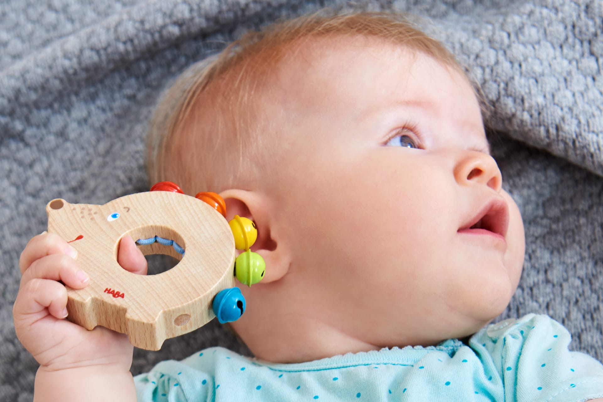 Sinneswahrnehmung bei Kindern | Baby hält Holzring mit Rassel von HABA ans Ohr