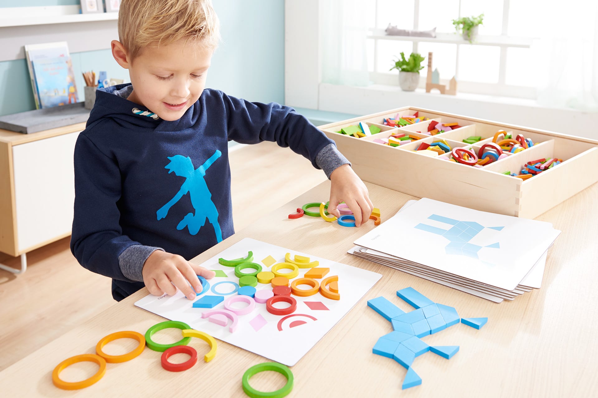 Fröbel Kindergarten | Junge mit blauen Sweatshirt legt Fröbel-Bilder mit bunten geometrischen Formen nach.