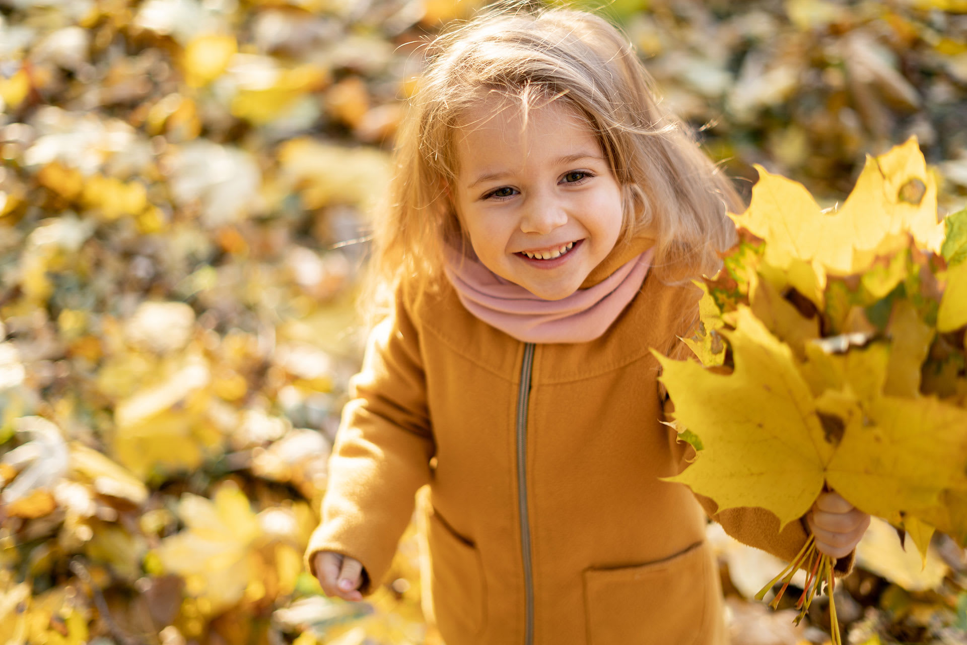 Kinder im Herbst richtig anziehen | Kind mit bunten Blättern in der Hand