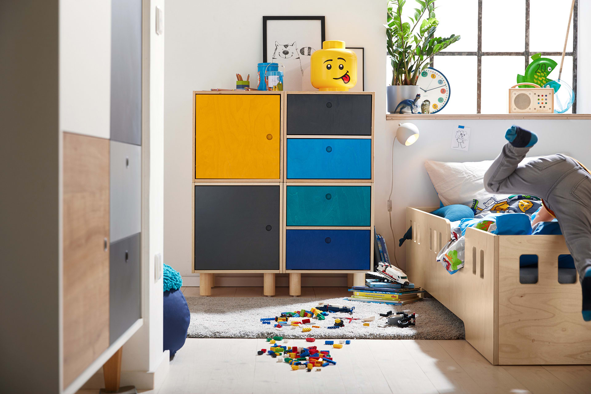 Kinderzimmer einrichten | Junge schmeißt sich in das Bett, Lego Steine liegen auf einem Teppich vor dem Bett