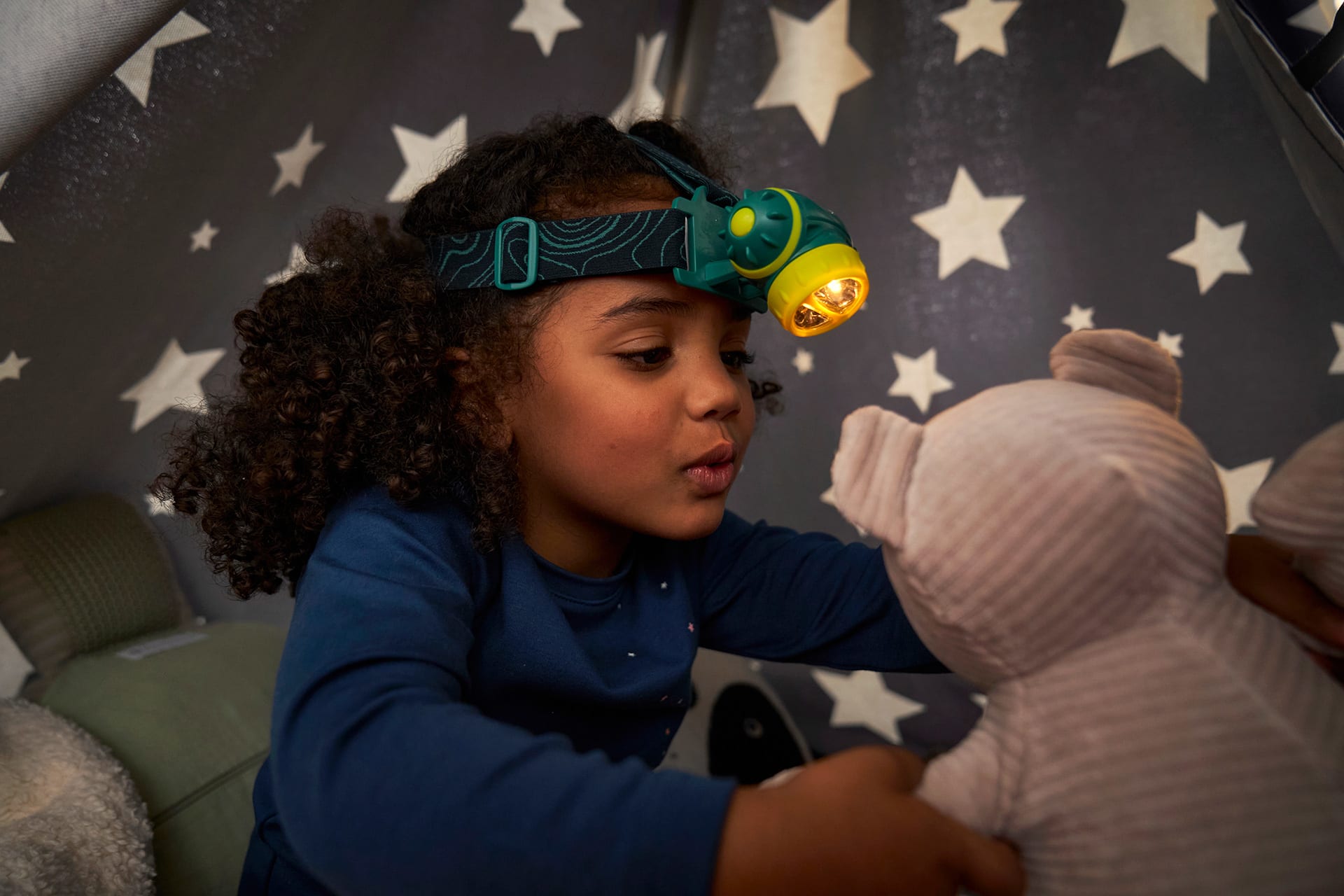 Rollenspiele | Mädchen hat Stirnlampe auf den Kopf und unterhält sich mit Teddy 