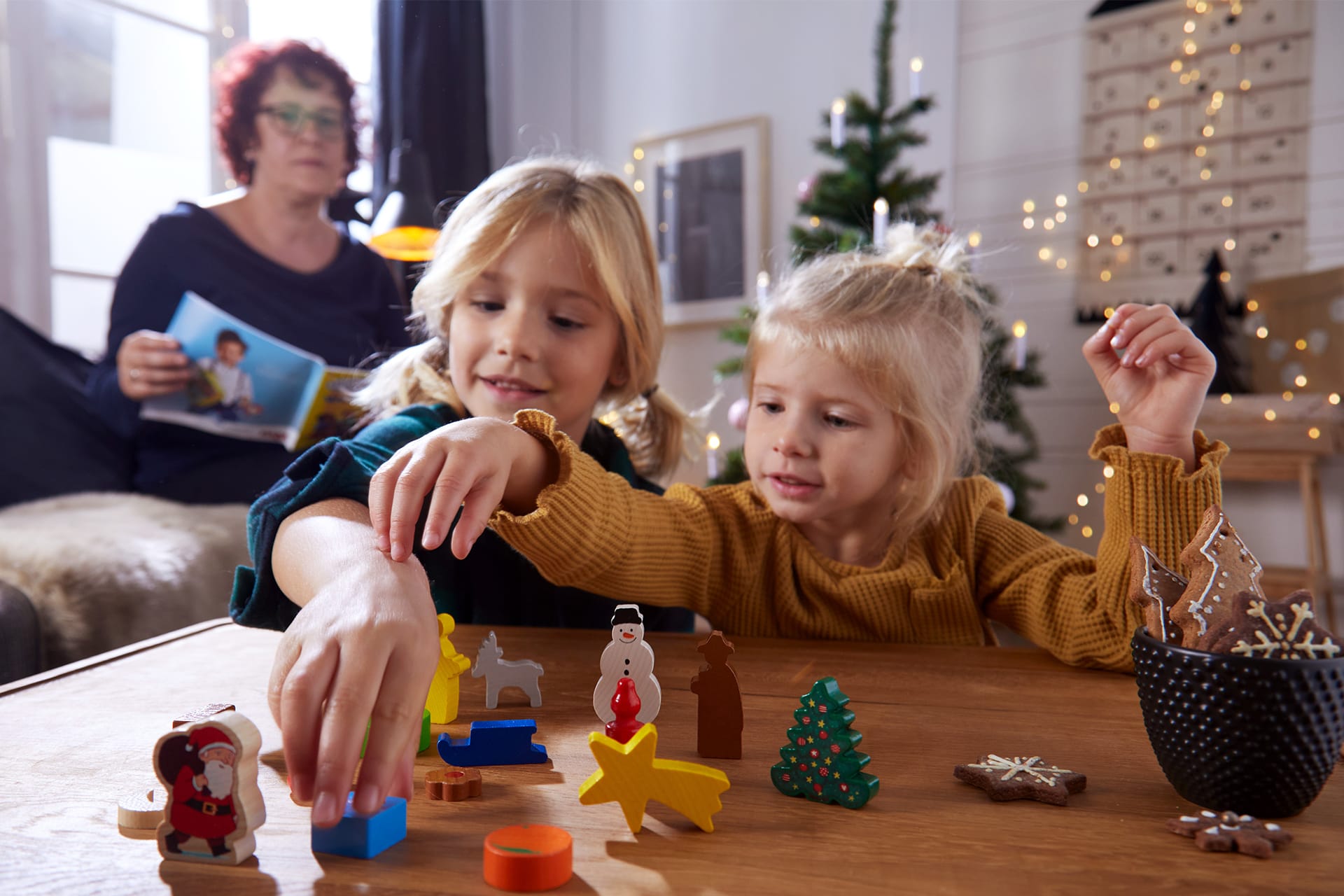  Exklusive Geschenketipps von HABA für das Weihnachtsfest | 2 Mädchen spielen mit Krippenfiguren. Frau liest eine Zeitschrift