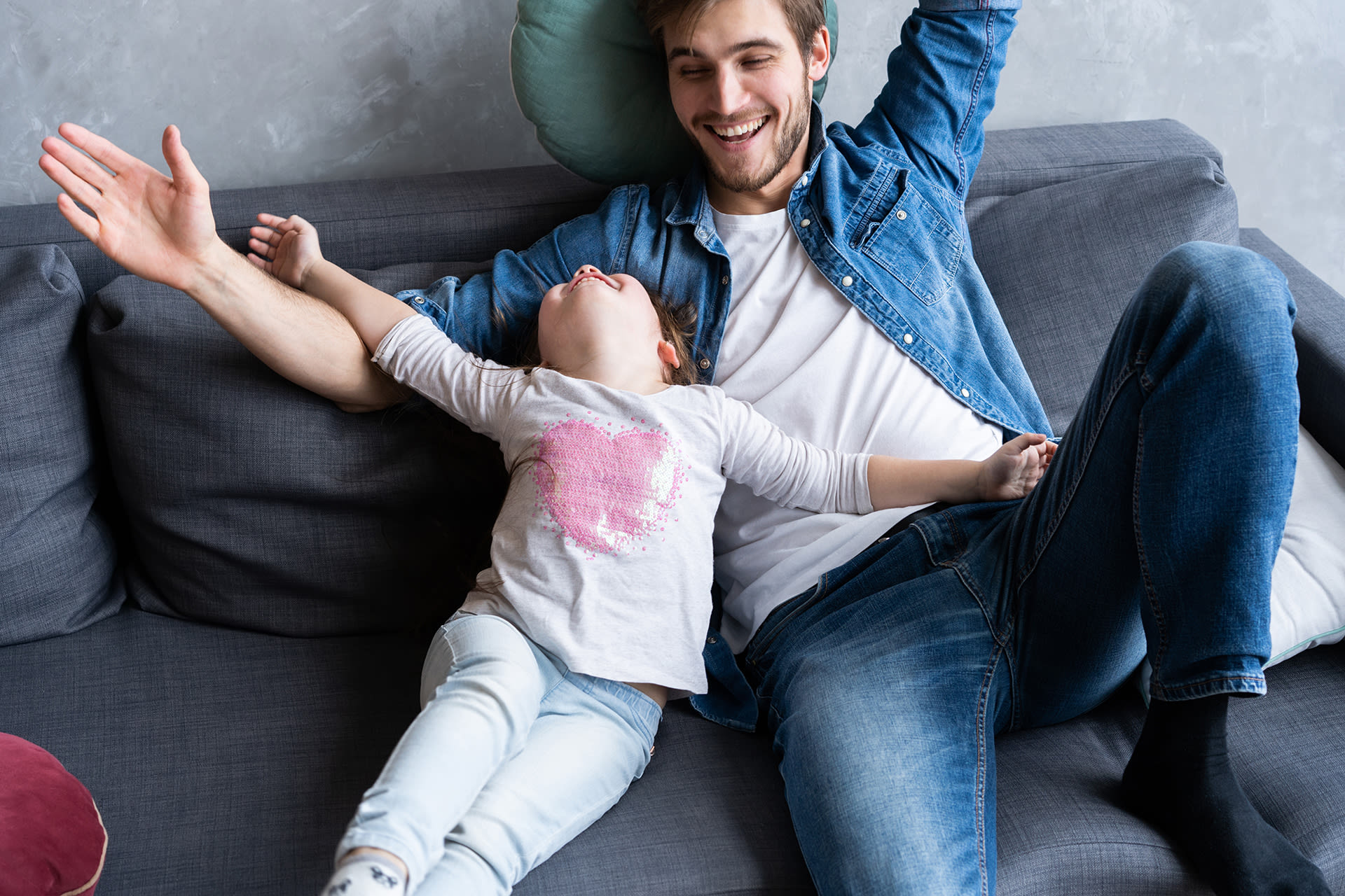 Erzählen für und mit Kindern | Papa und Tochter liegen auf dem Sofa mit ausgebreiteten Armen