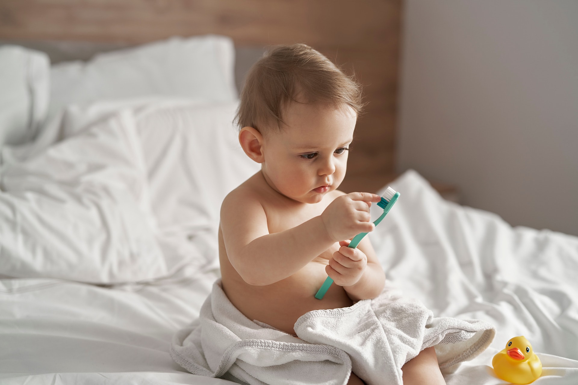 Spielerisch lernen | Baby sitzt im Bett und hat Zahnbürste in den Händen
