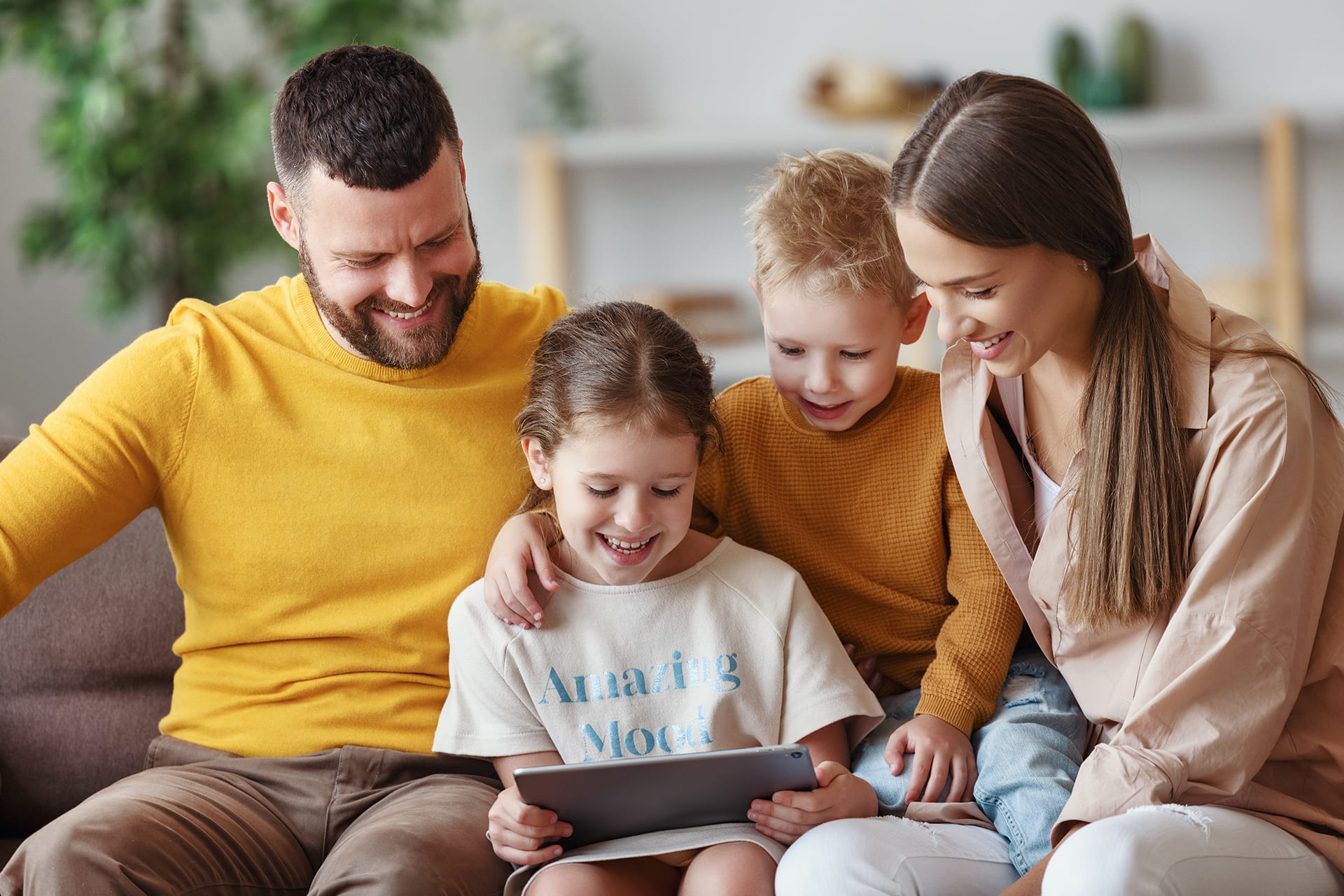 Tablets für Kleinkinder | Zwei Kinder und Eltern sitzen auf dem Sofa und schauen auf ein Tablet 