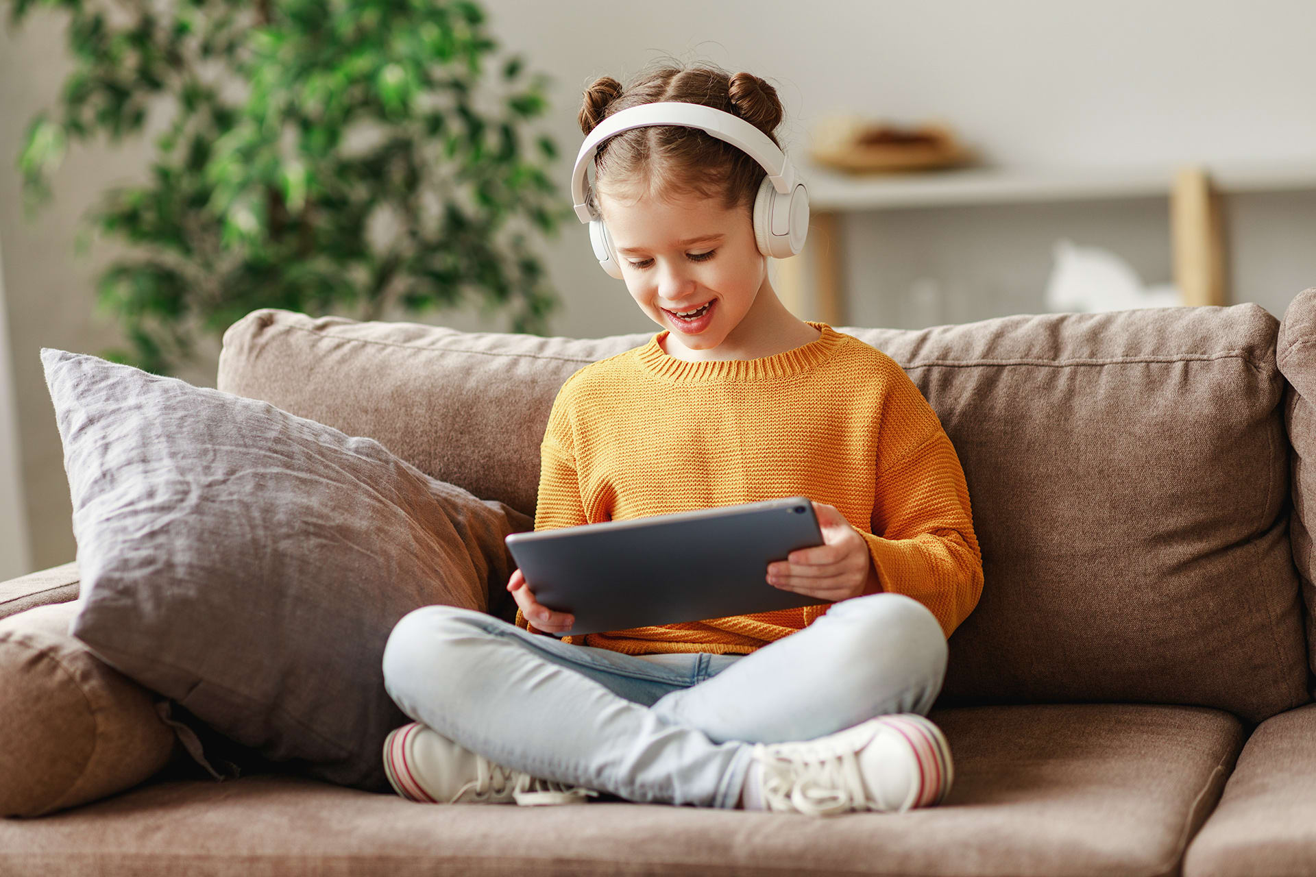Tablets für Kleinkinder | Mädchen sitzt mir Kopfhörern und Tablet auf dem Sofa 