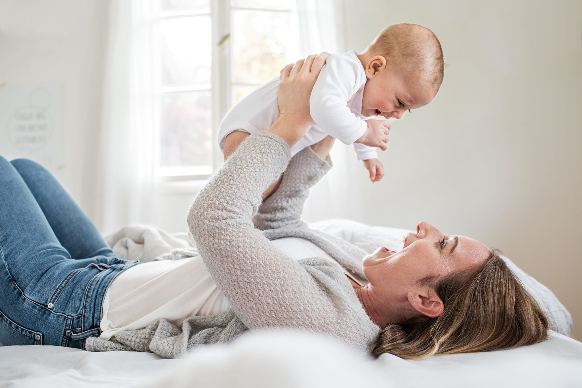 Baby zum Lachen bringen | liegende Mutter hält lachendes Baby in die Luft