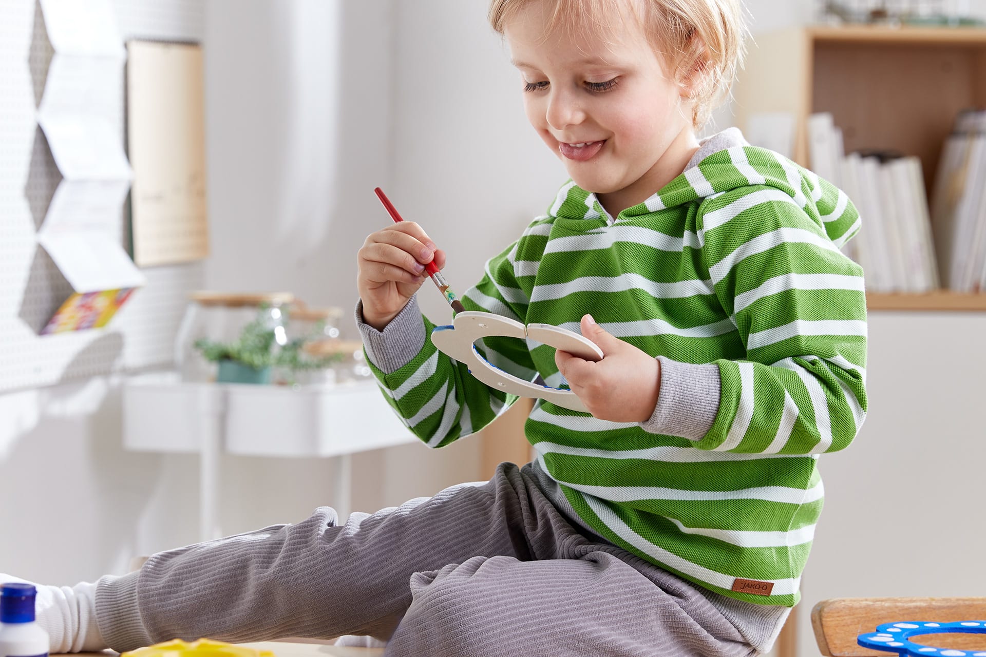 Insektenhotel mit Kindern bauen | Kleinkind in grün-weiß geringeltem Shirt malt Holzblume an