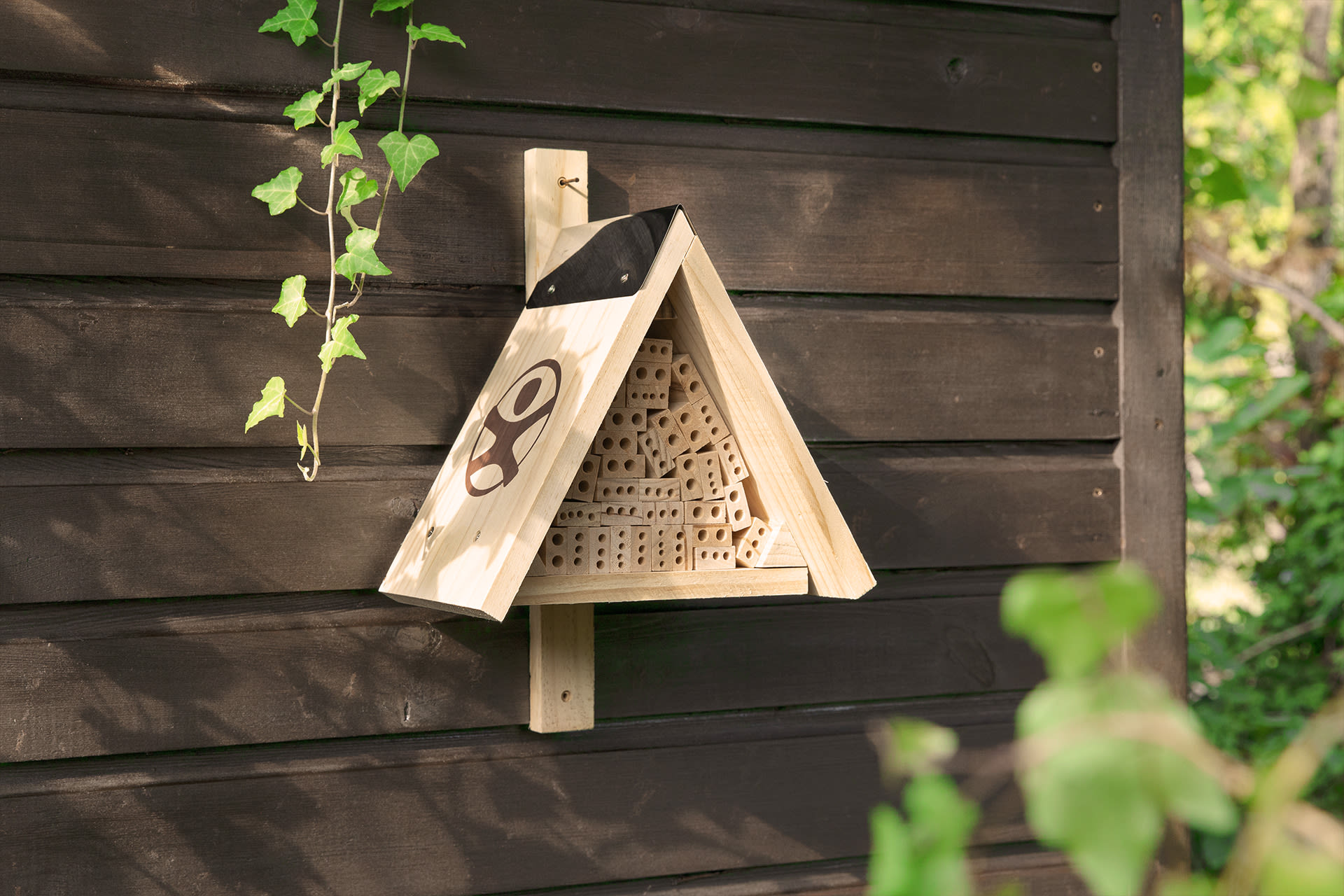  Insektenhotel mit Kindern bauen | dreieckiges Insektenhotel hängt an einer Holzhütte