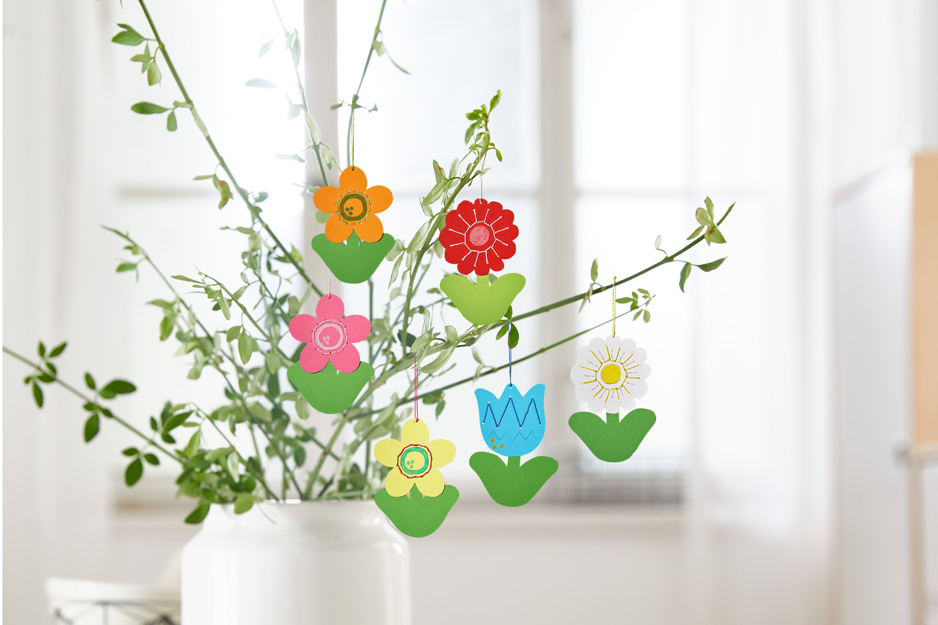 Blumen basteln mit Kindern | Gebastelte Papierblumen hängen an einem Strauß aus Ästen