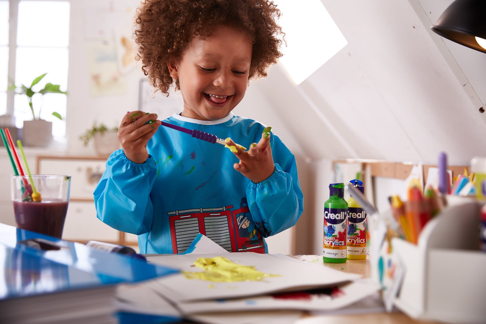  Fingerfarben-Ideen Kinder | Junge mit blauer Malschürze malt sich seine Finger gelb an