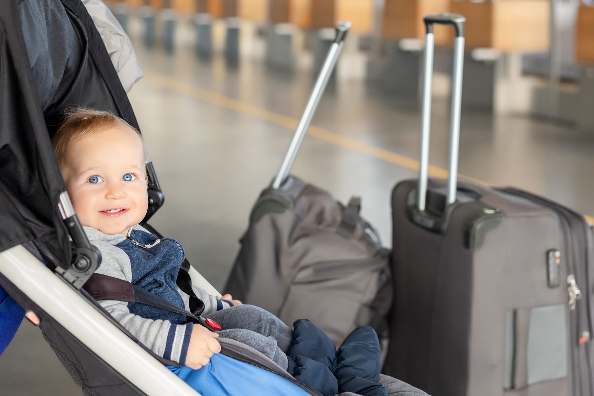 Fliegen mit Baby | Baby Junge sitzt im Kinderwagen in der Nähe von Gepäck