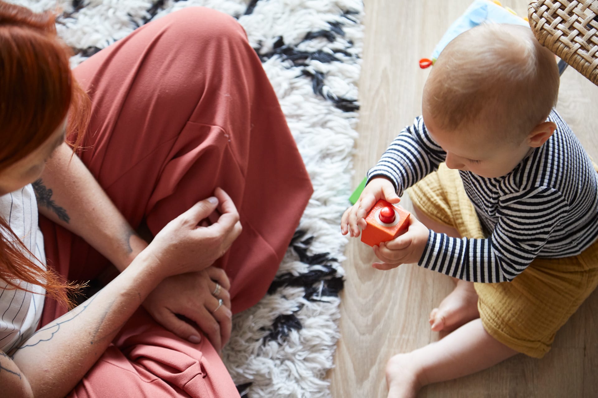 Feinmotorik fördern | Baby mit Bauklötzchen in Händen, sitzt mit Mama auf dem Fußboden