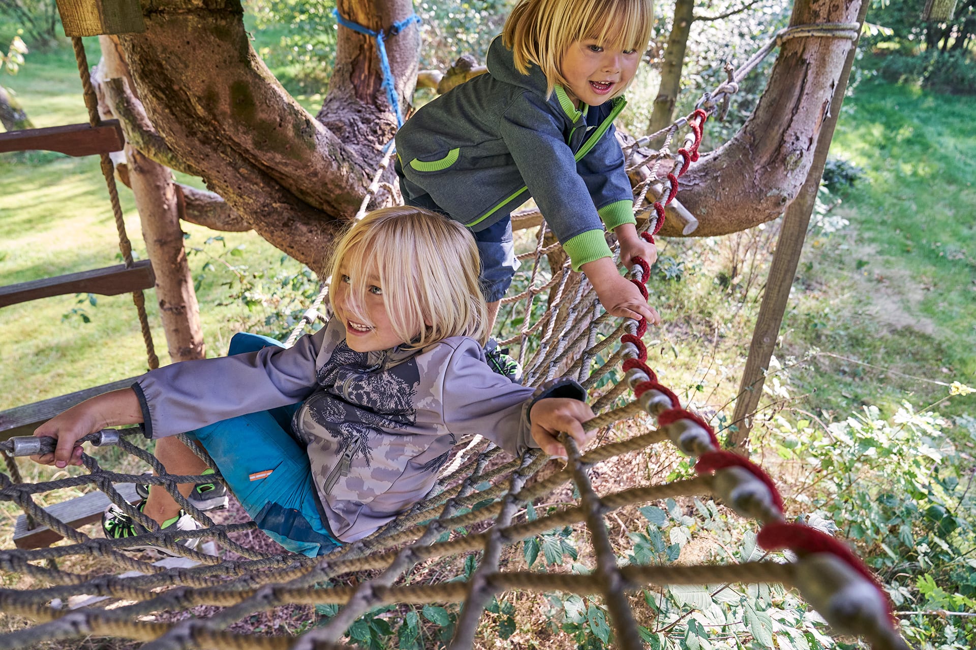 Spiele für draußen | Zwei Kinder klettern zwischen Bäume über Seile