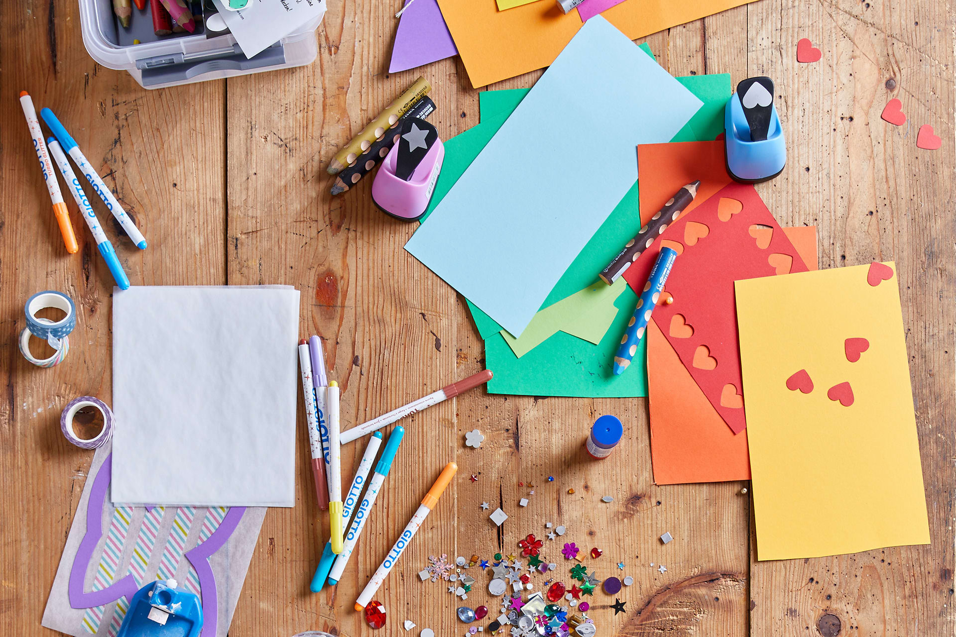 Geschenke basteln | Bastelmaterialien, bunter Tonkarton, Glitzersteine, Buntstifte, Motivlocher liegen auf einem Tisch