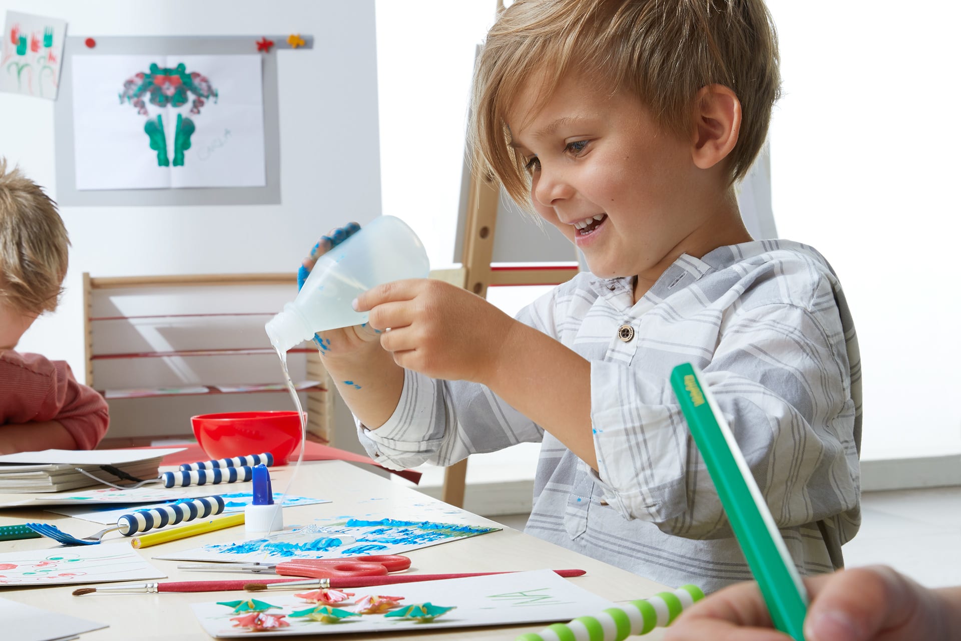 Geschenke basteln | Kind bastelt am Tisch, klebt Schnipsel auf eine Karte