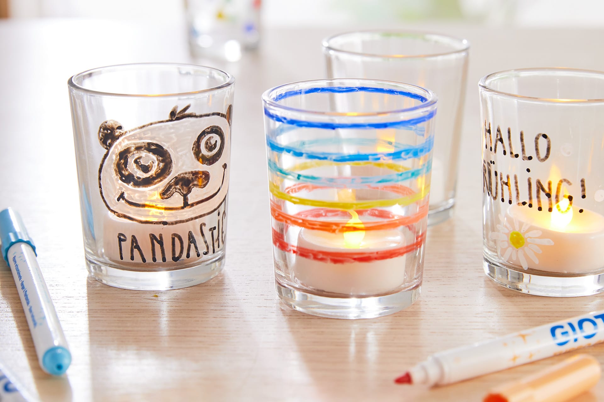 Geschenke basteln | Bemalte Gläser mit Pandagesicht, bunte Streifen und Text, Teelicht innen