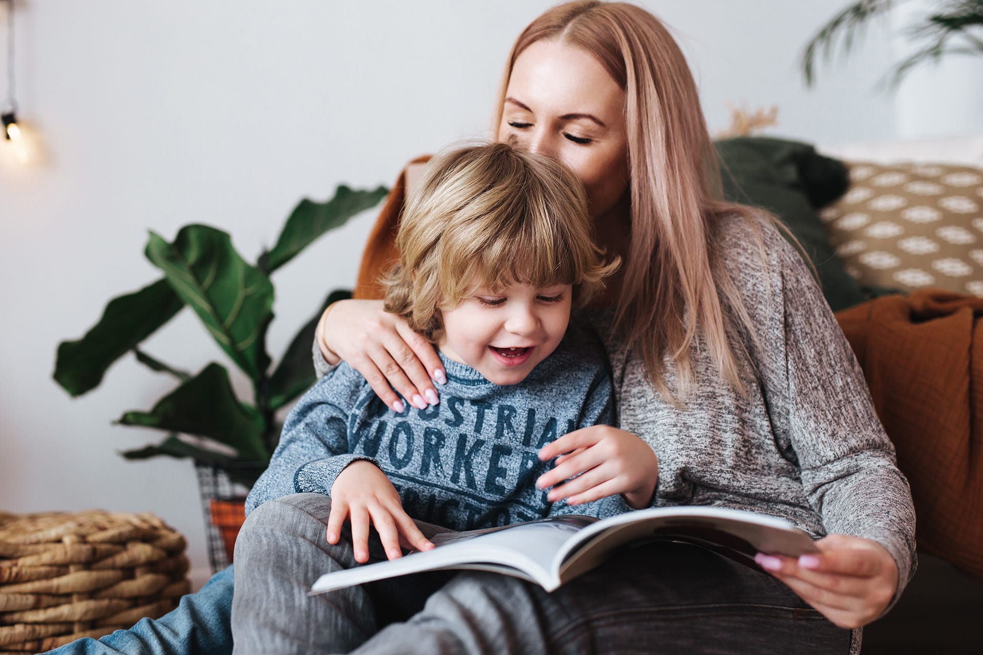 Sprachförderung | Mutter und kleiner Sohn sitzen zusammen und lesen ein Buch zu Hause 