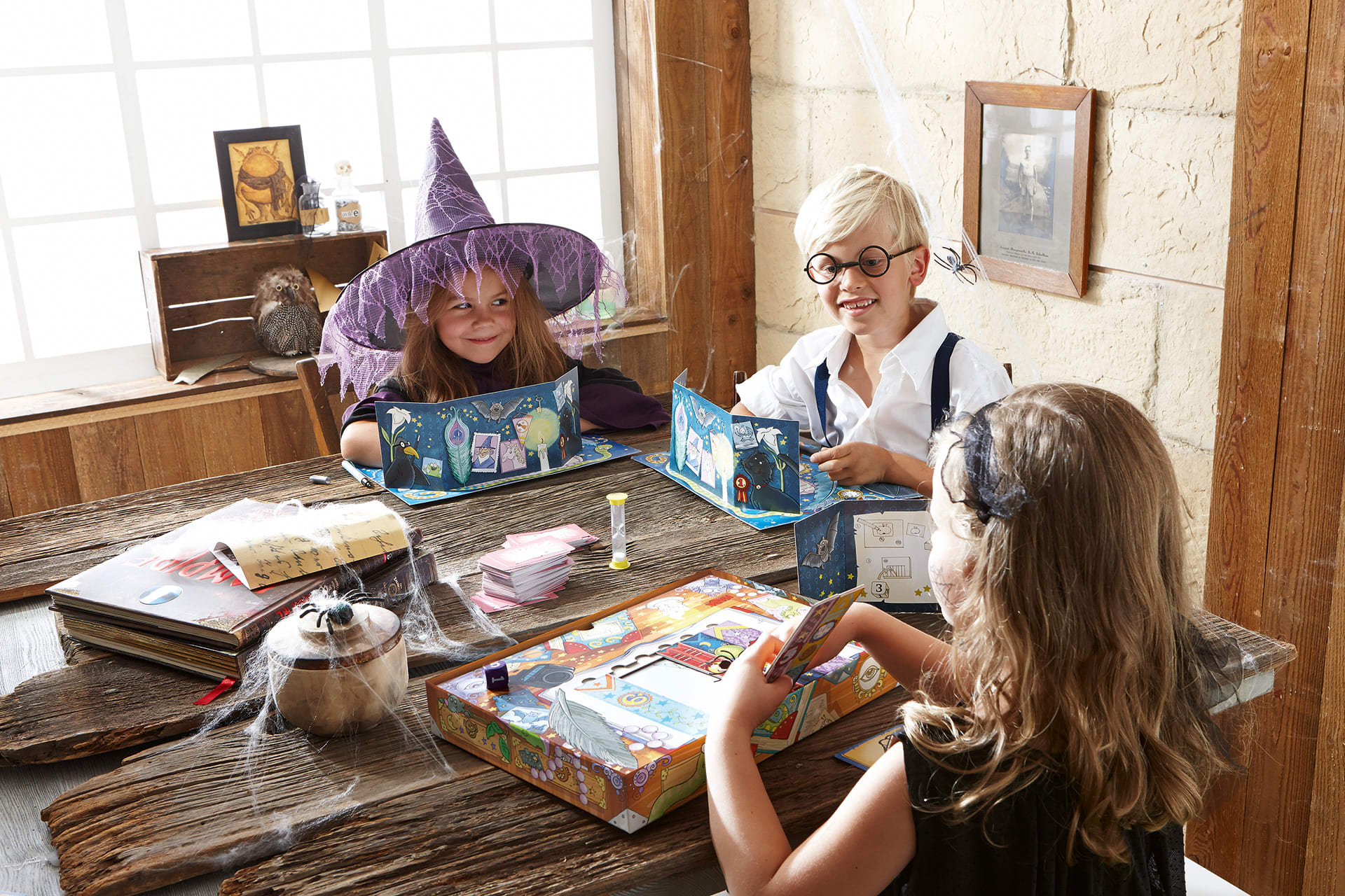 Halloween Spiele | Drei Kinder in Halloween-Kostümen sitzen am Tisch und machen ein Spiel 