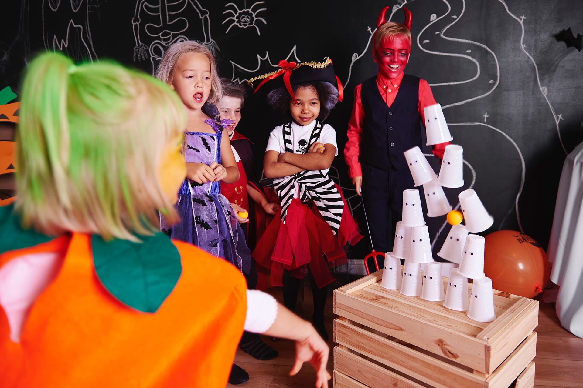 Halloween Spiele | Kinder in Halloween-Kostümen werfen auf Geister-Becher-Turm mit einem Ball 
