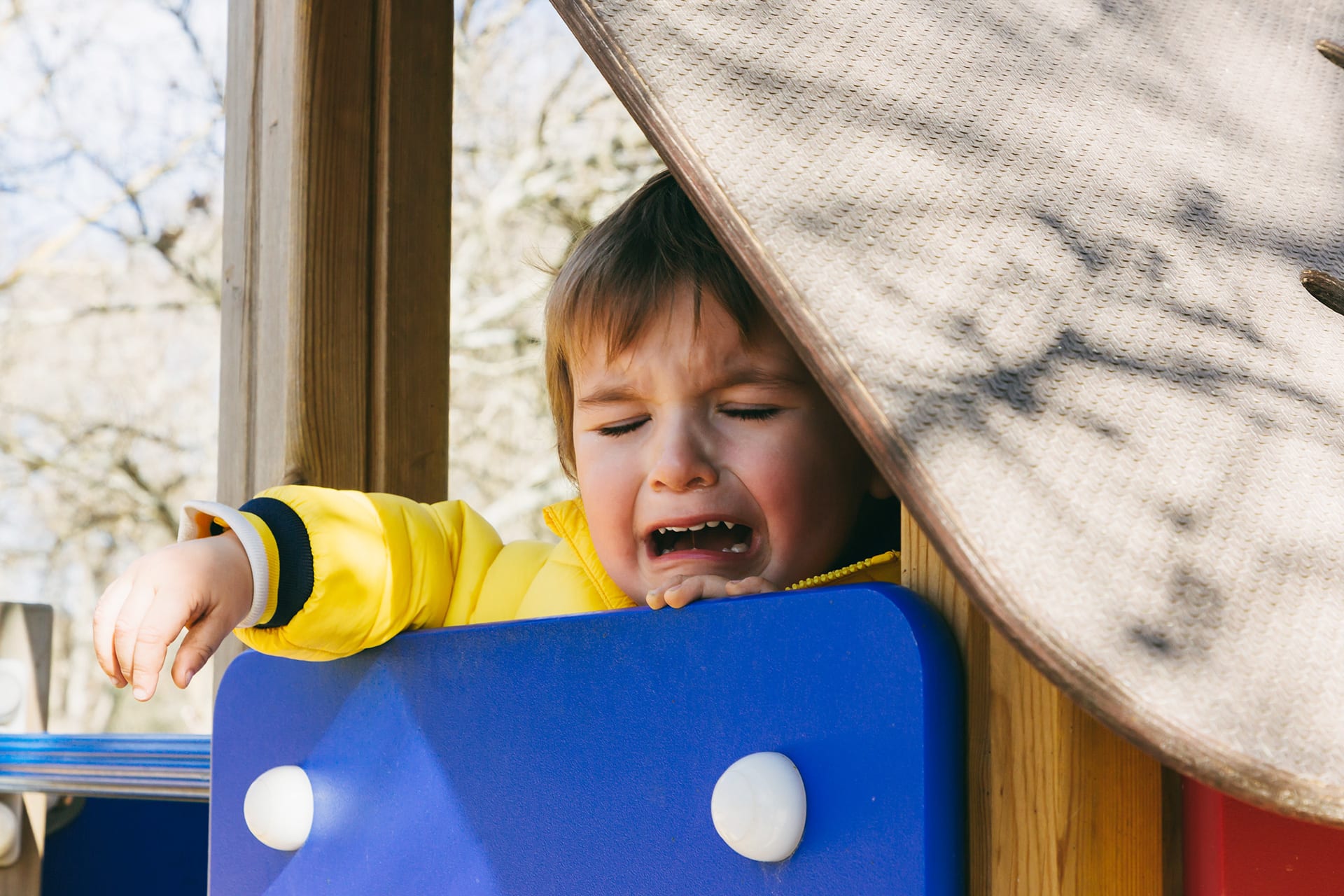 Trennungsangst bei Kindern | kleiner Junge weint, während er auf einer Rutsche auf dem Spielplatz sitzt