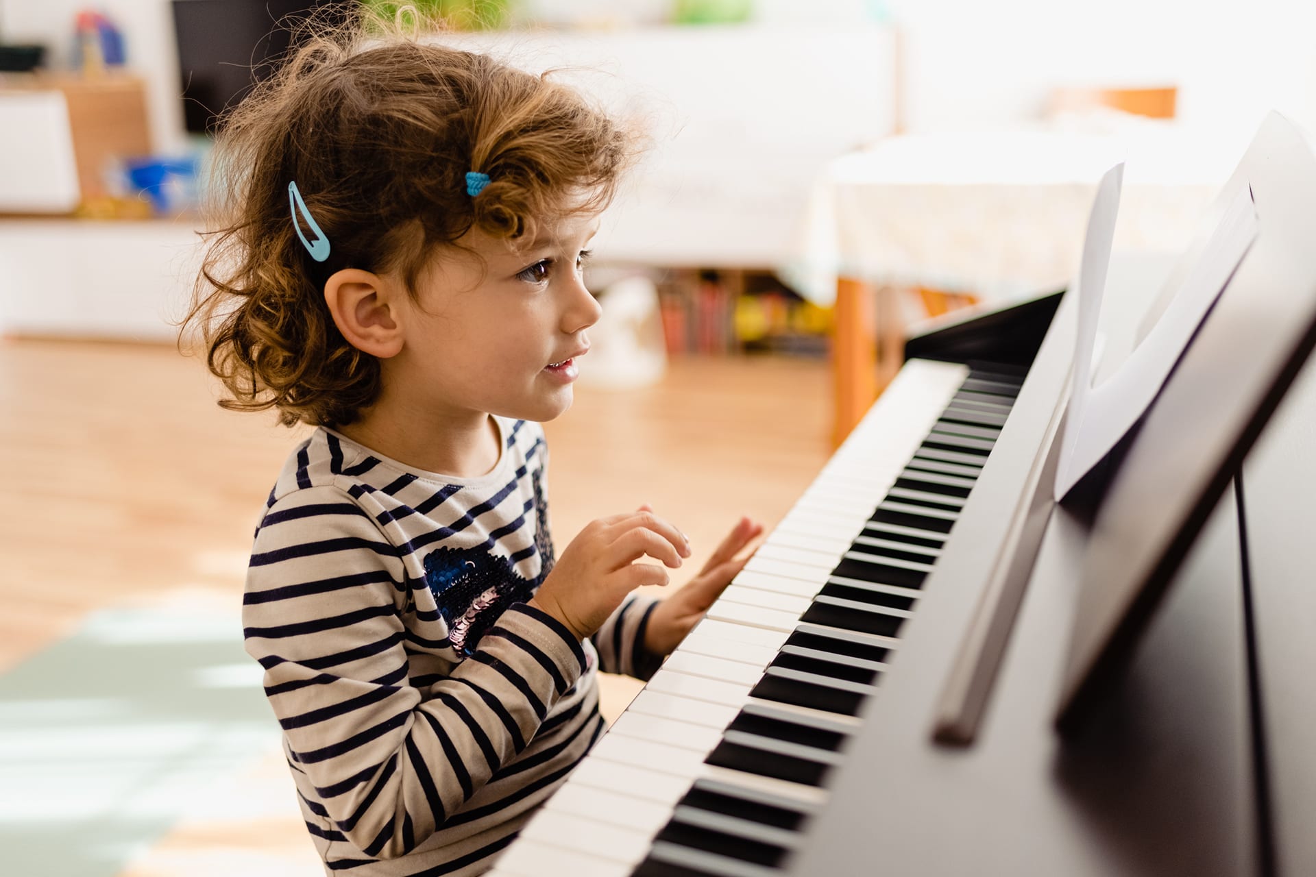  Welches Instrument für mein Kind | kleines Mädchen sitzt am Klavier und experimentiert lächelnd mit Musiknoten