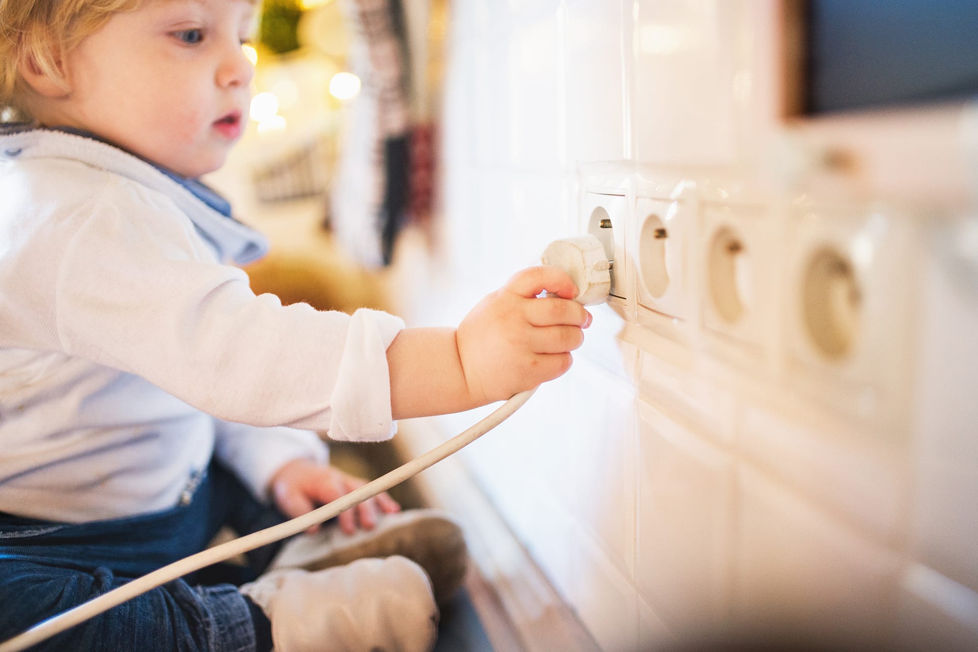 Kindersicherheit Zuhause | Baby sitzt vor Steckdosenleiste, steckt Kabel ein