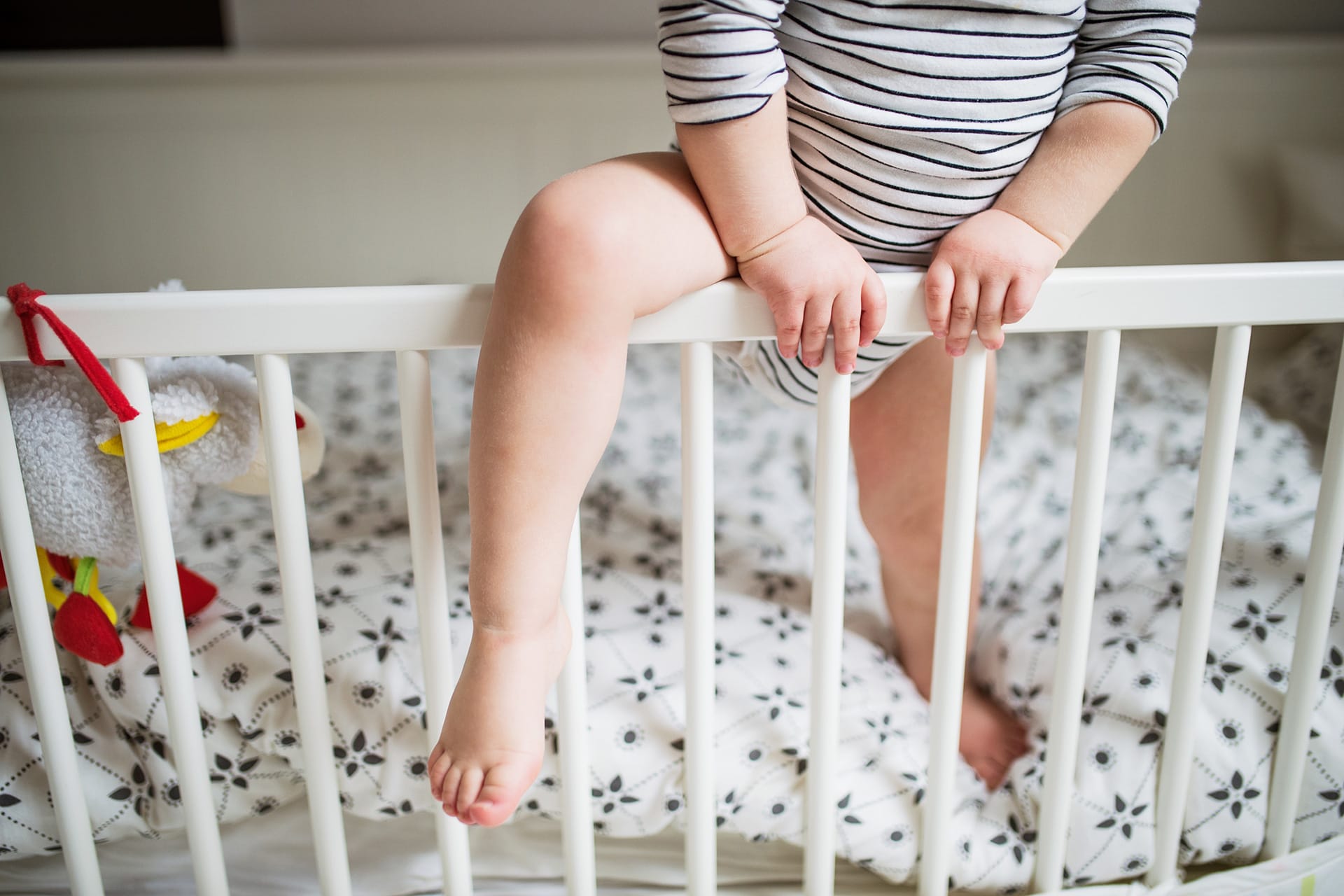 Baby steht im Gitterbett | Baby mit Bein über Gitterbett-Stangen
