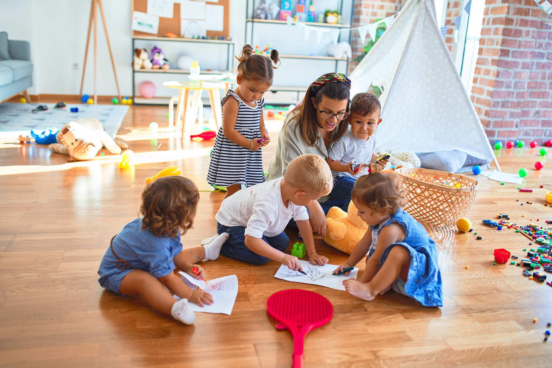 Kita Gebühren, Kindergarten Kosten | Krippen-Kinder sitzen mit Erzieherin am Boden und malen