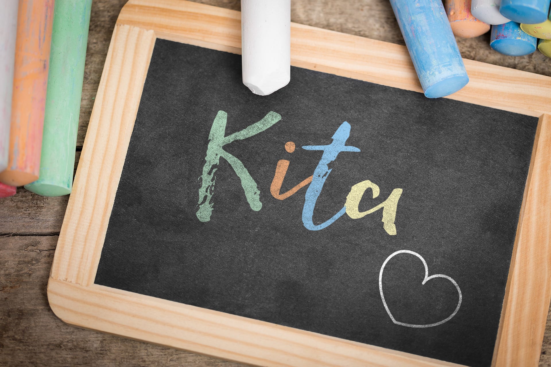 Kita Gebühren, Kindergarten Kosten | Auf einer Schiefertafel steht mit bunter Kreide Kita geschrieben