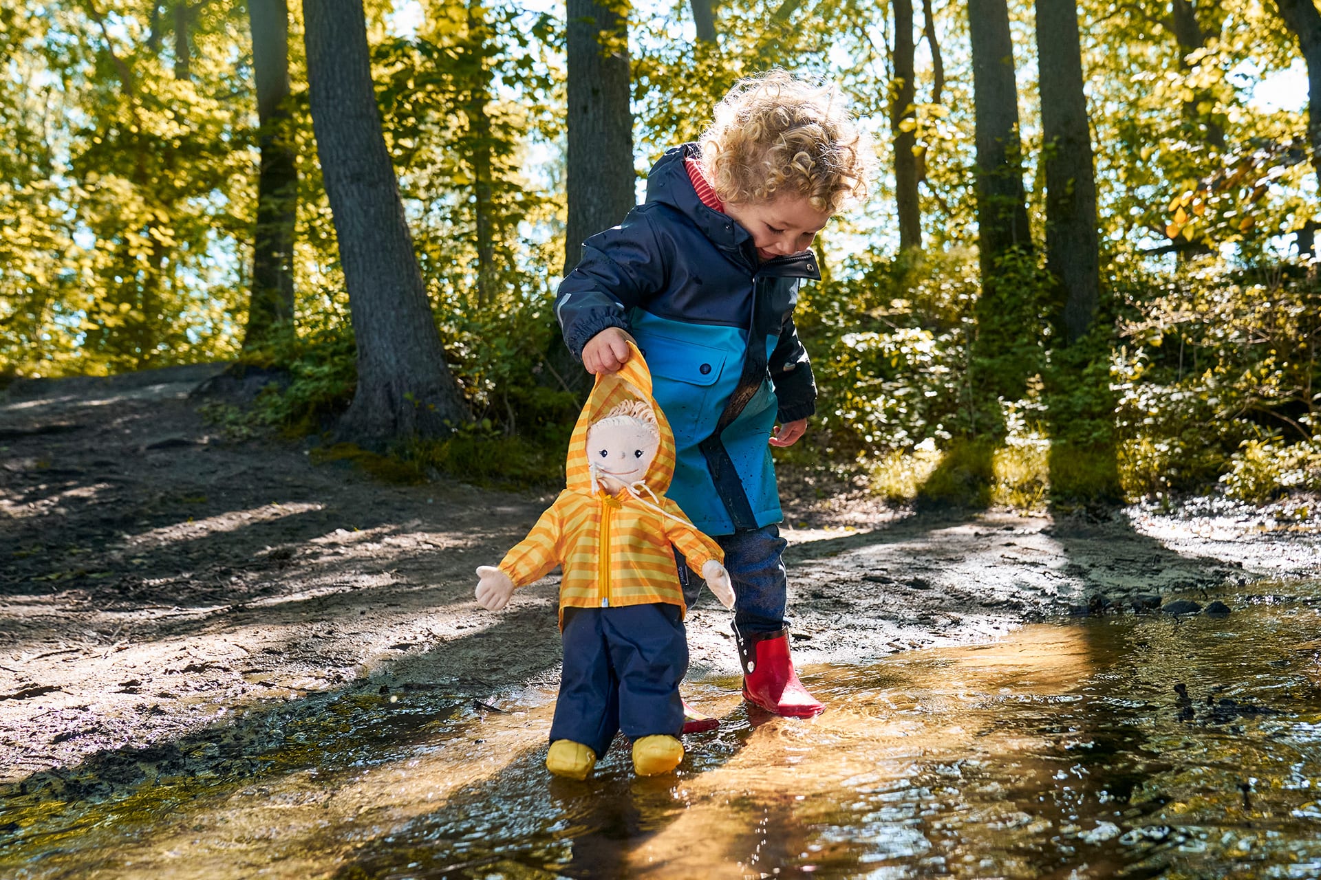 Spiele für draußen | Kind in Gummistiefeln, Matschjacke steht im  Wald im Bach und hat Puppe Krümel in der Hand