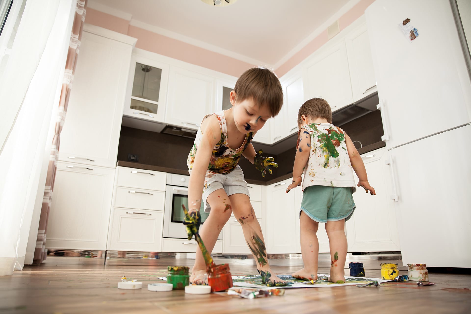 Erziehungshilfe | zwei Jungen malen mit Händen, Füßen und Pinsel auf Papier, am Küchenboden