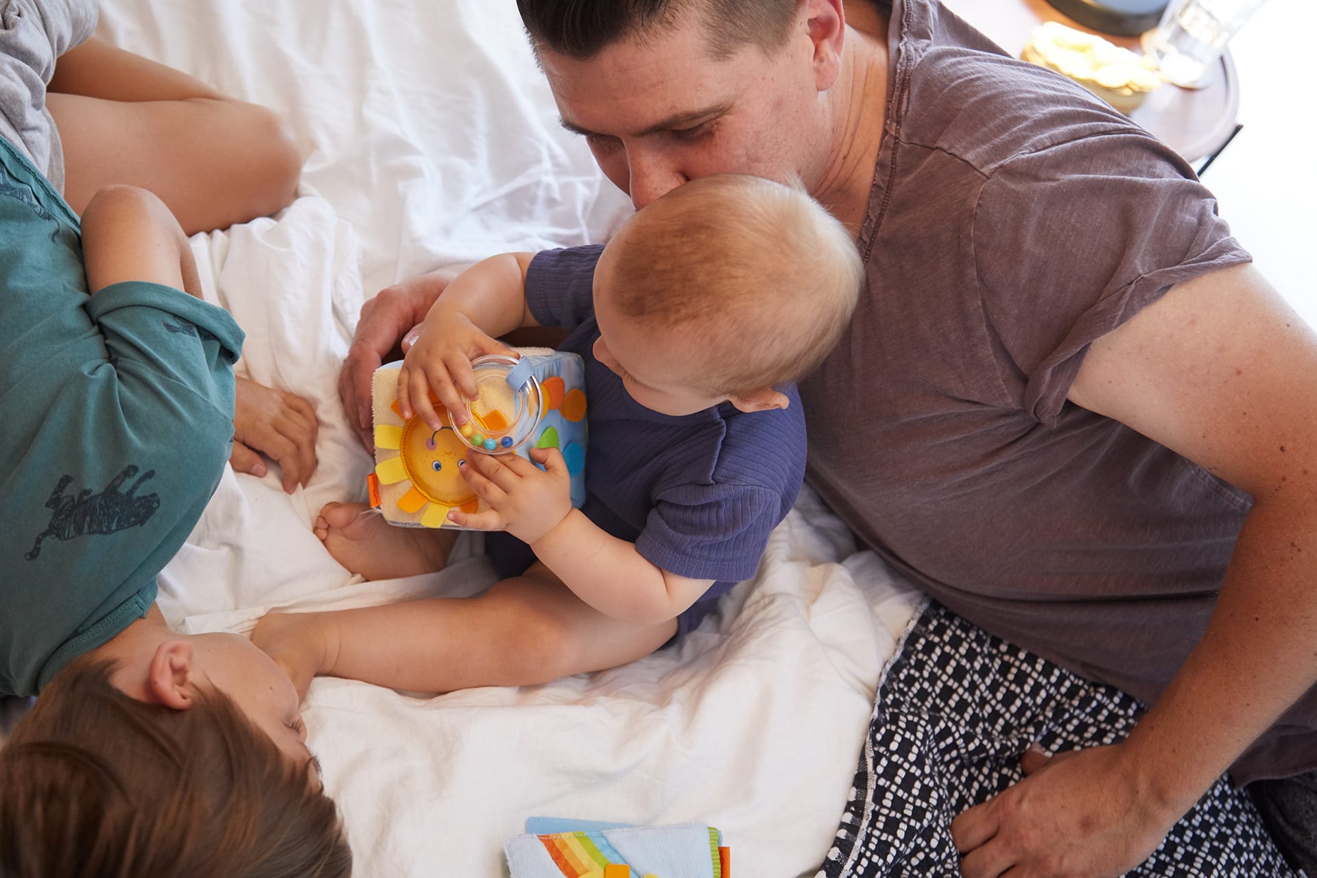 Warum spielen wichtig ist | Vater sitzt hinter Baby und schaut ihm zu wie er mit Würfel spielt 